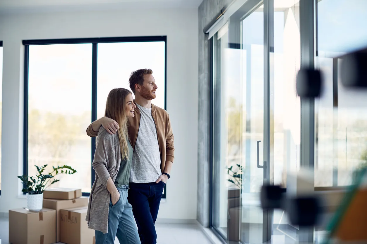 Wohnkomfort und Lebensqualität durch Energieeffizienz mit einem Energieeffizienz-Experten München Ein junges Paar in einem modern gestalteten, lichtdurchfluteten Raum mit großen Fenstern und Kartons im Hintergrund, repräsentiert die Vorteile einer professionellen Energieberatung München.