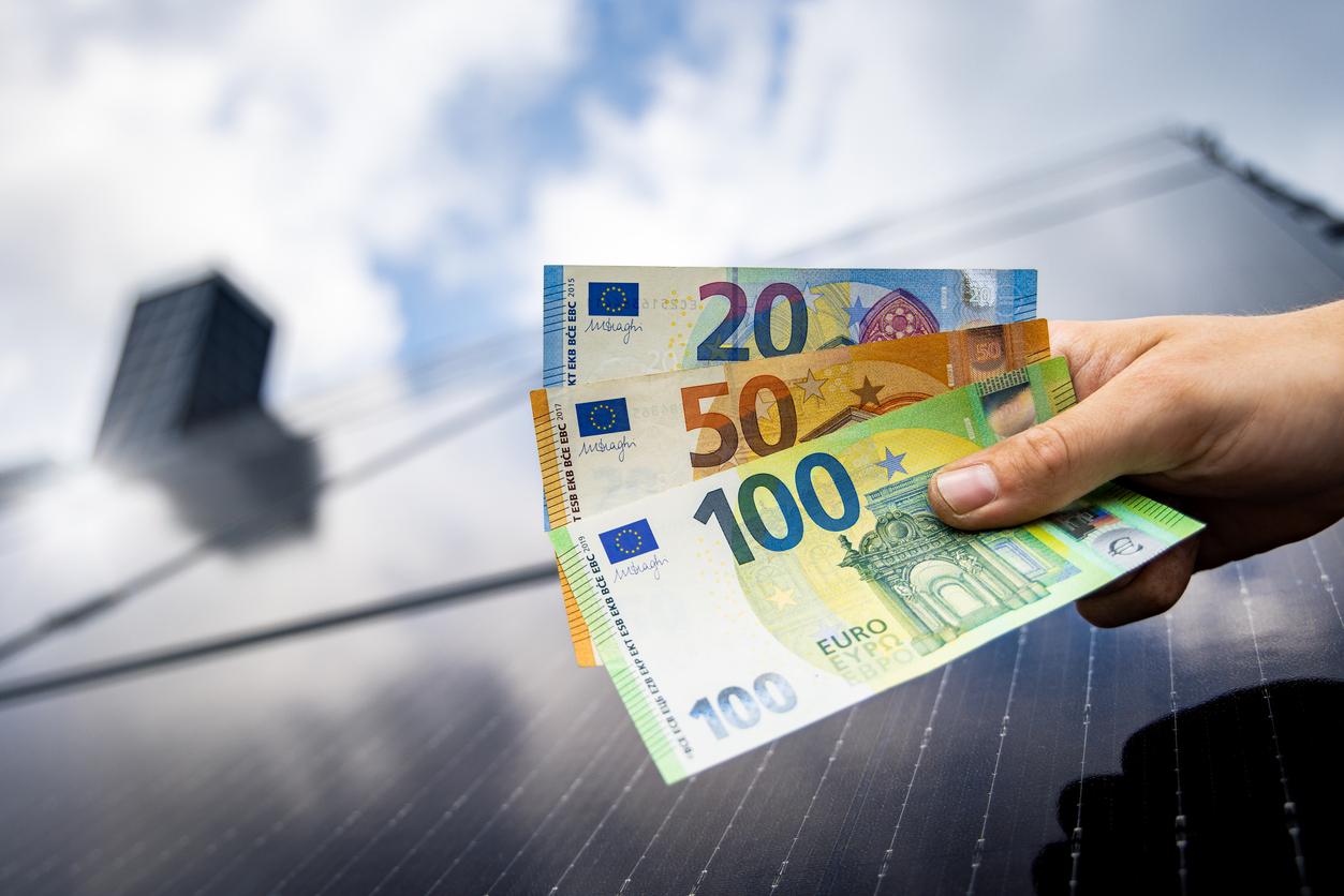 Fördermittel und Finanzierung für energetische Maßnahmen. Hand mit Euro-Geldscheinen vor Photovoltaikanlage als Symbol für Investition in Energieeffizienz