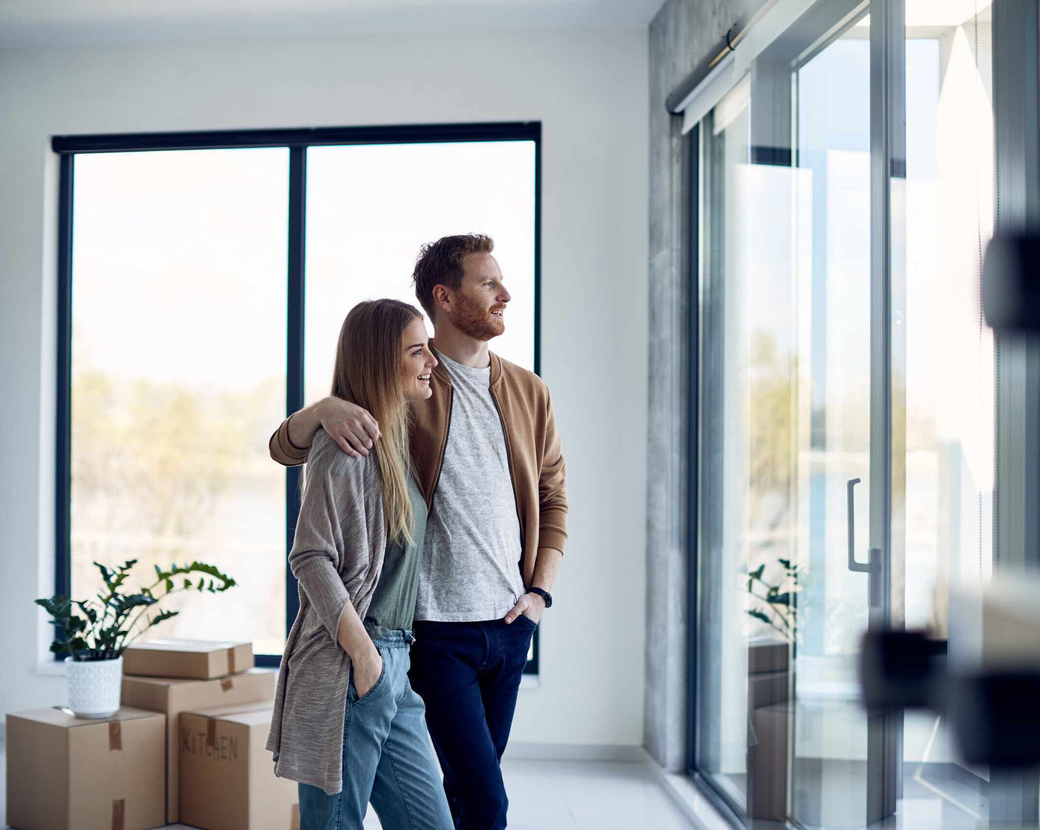 Junges Paar steht glücklich in ihrem neuen, energieeffizienten Zuhause mit großen Fenstern.