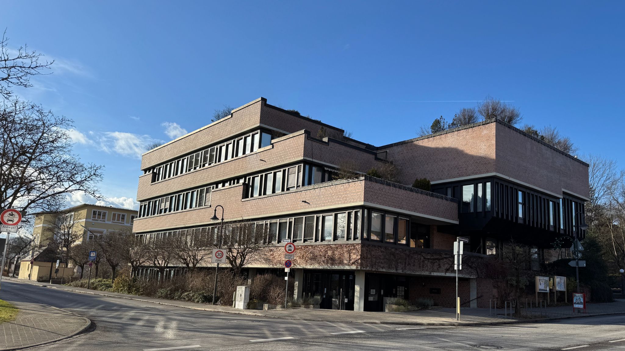 Gemeindegebäude in Gauting bei strahlendem Sonnenschein, umgeben von Bäumen und einer ruhigen Straße.