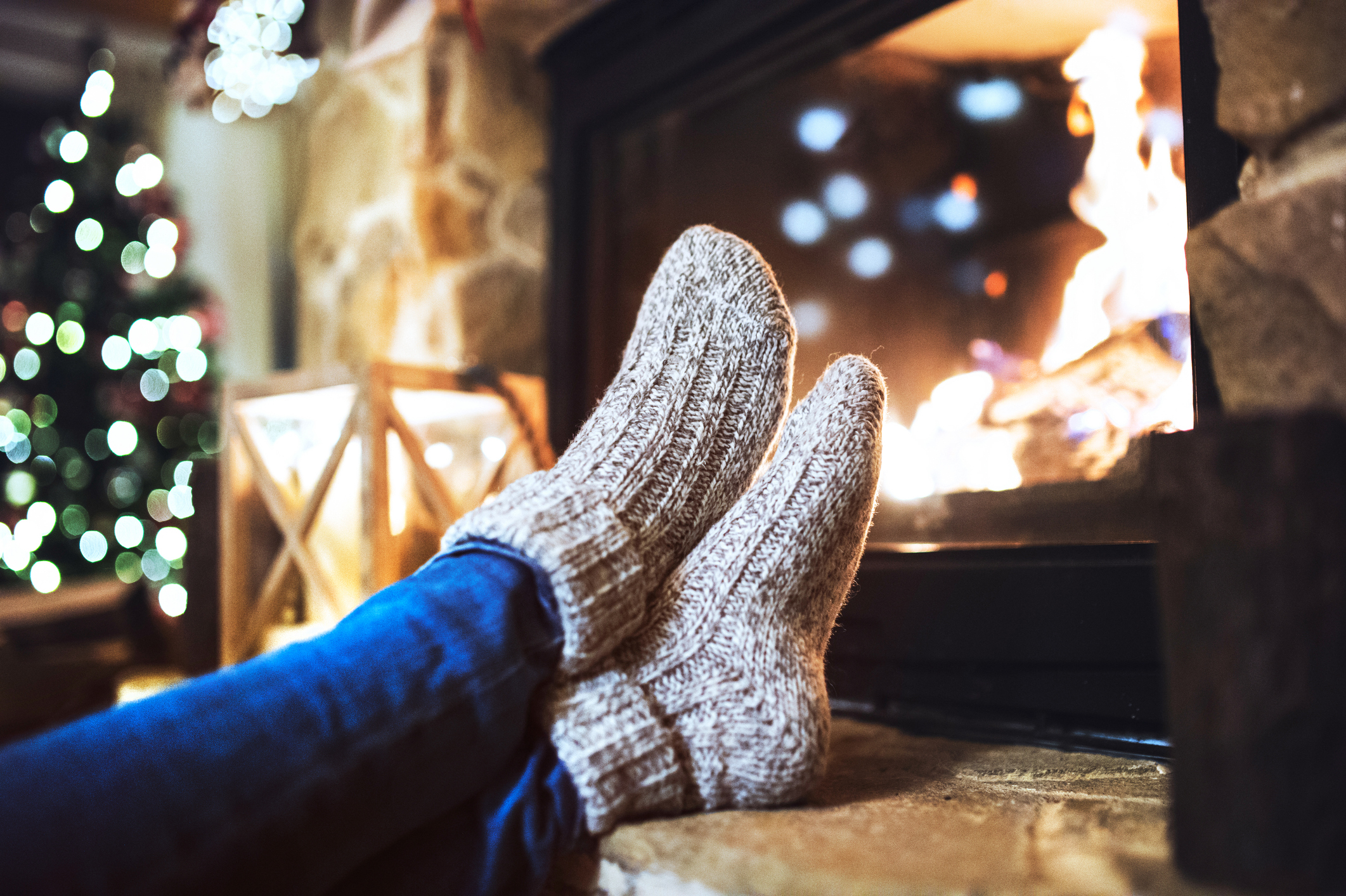 Gemütliche Szene vor einem Kaminfeuer mit warmen Wollsocken und Weihnachtsbaum im Hintergrund.