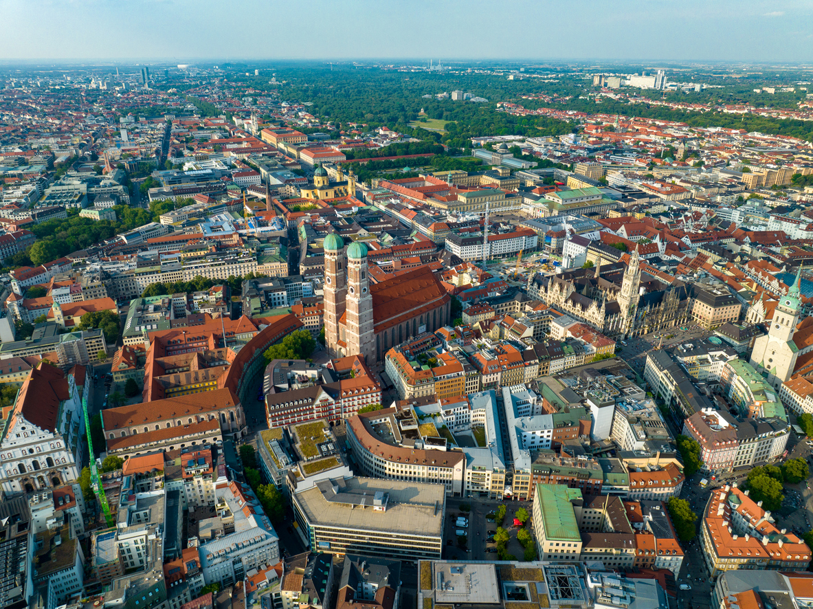 Luftaufnahme von München, die das Stadtzentrum mit wichtigen Gebäuden und umliegenden Grünflächen zeigt.