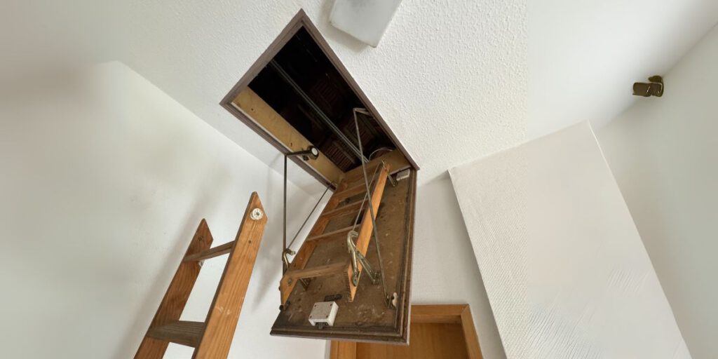 Ungedämmte Bodentreppe mit Holzleiter in geöffneter Deckenöffnung zu einem unausgebauten Dachboden